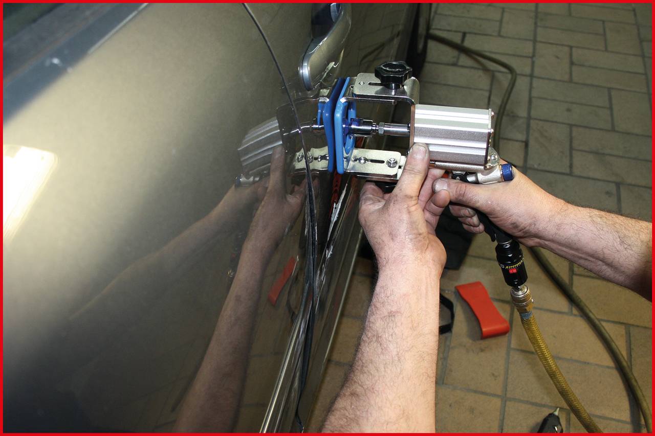 Mechanik opravuje promáčklinu na autě pomocí speciálního nástroje.