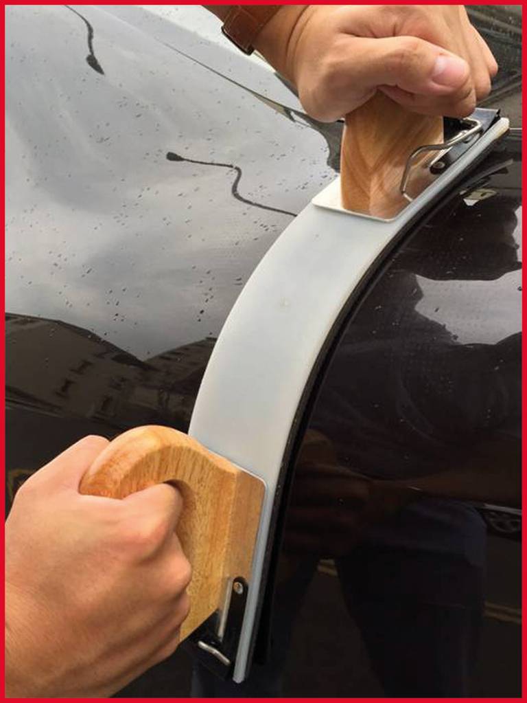 Dvě ruce drží dřevěné rukojeti připevněné k velkému přísavkovému držáku, který je umístěn na povrchu automobilu.