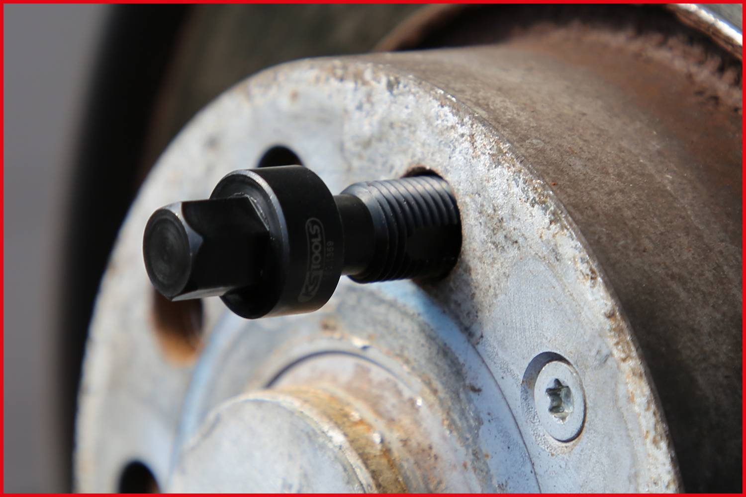 Nářadí k demontáži ložiska kola, nasazené v těsné blízkosti na zrezavělém náboji kola. Zaměření na šroubovací mechanismus.