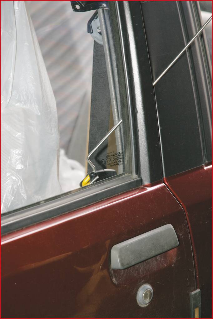 Obrázek ukazuje detailní záběr autového okna. Drát je používán k odemčení dveří. Lak automobilu je rezavě hnědý.