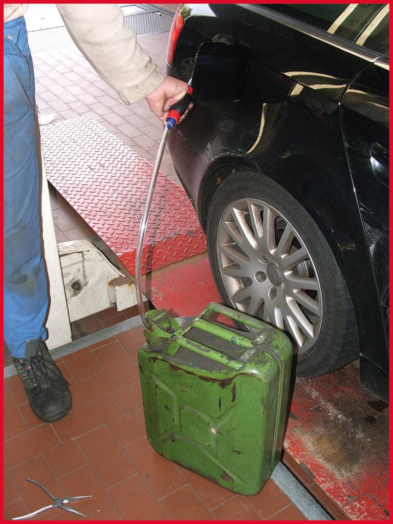 Osoba nalévá palivo z zelené nádoby do černého automobilu. Auto stojí v autodílně na zvedáku.