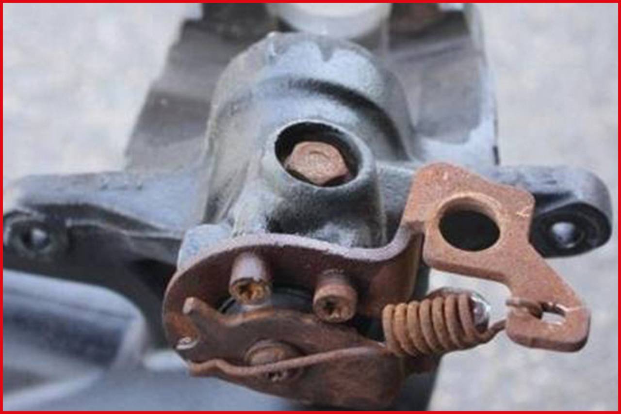 Detailní záběr mechanické autosoučástky, pravděpodobně brzdy, s rezavými kovovými komponenty a šroubovou pružinou.