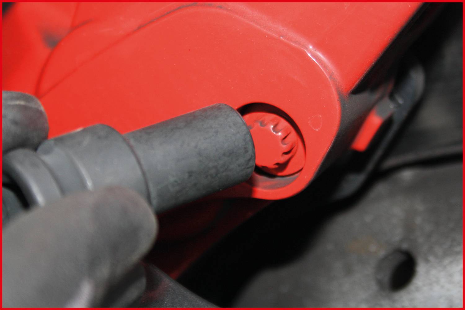 Detailní záběr ruky v rukavici, která upevňuje nebo uvolňuje černý nástroj na červené mechanické součásti.
