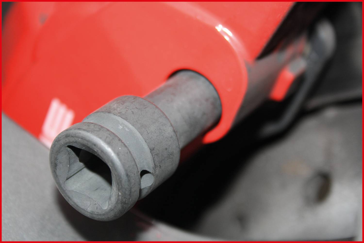Detail palivové pistole červené barvy zasunuté do plnicího hrdla automobilu. Snímek zachycuje výdejní pistoli a oblast palivové nádrže vozidla.