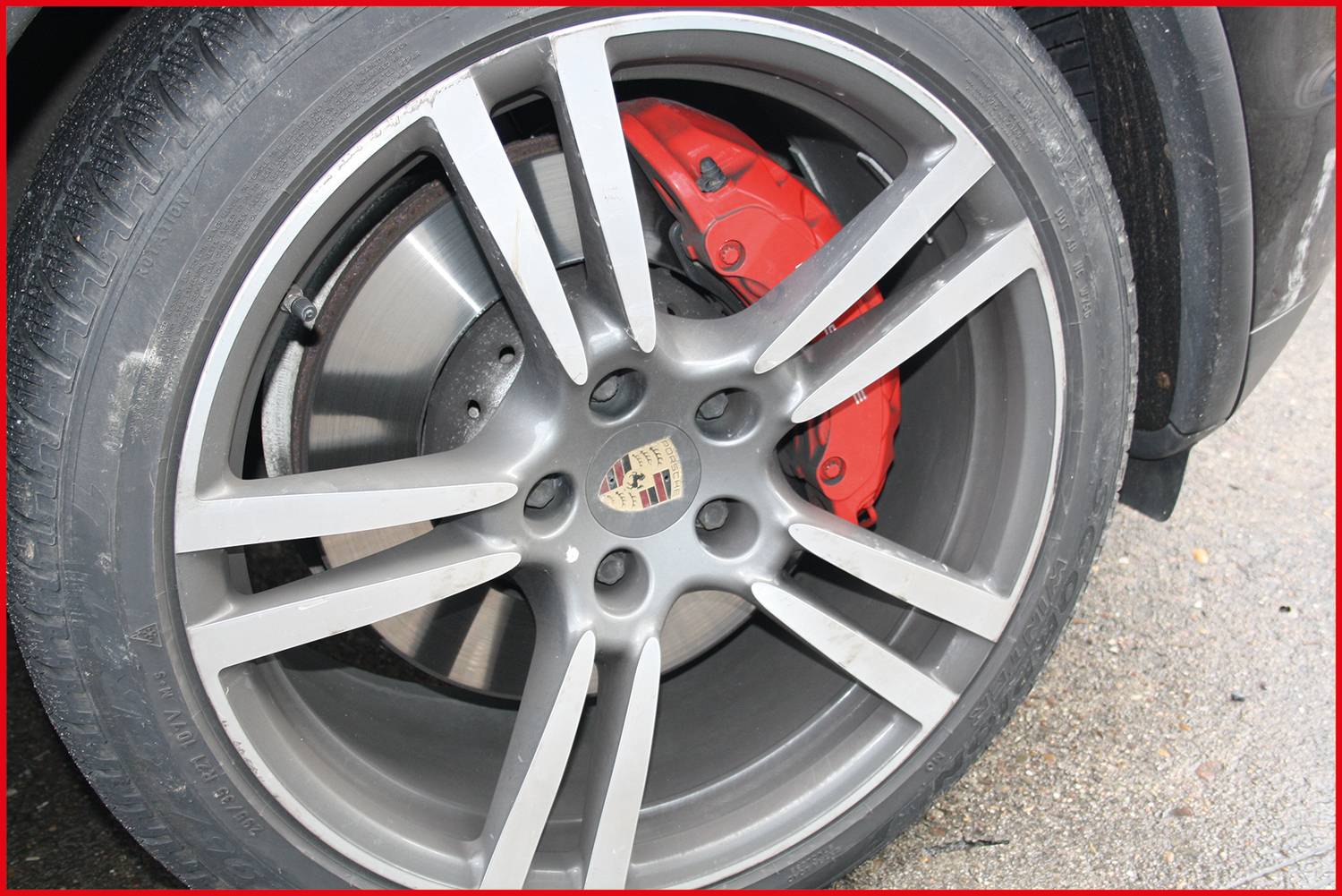 Detailní záběr pneumatiky automobilu se stříbrným diskem a červeným brzdovým kotoučem za diskem. Logo značky viditelné uprostřed.