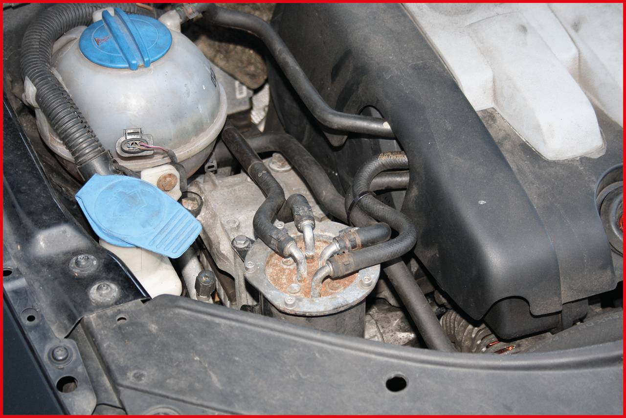 Motorový prostor automobilu s nádobkou chladicí kapaliny a různými hadicemi a vedením. Hlavní komponenty jsou uspořádány viditelně.