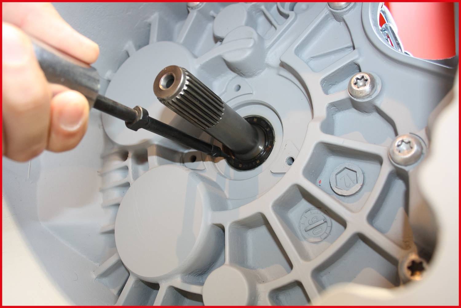 Detailní záběr ruky, která drží nástroj a pracuje na mechanické spínací komponentě. Jsou viditelné šrouby a ozubená kola.