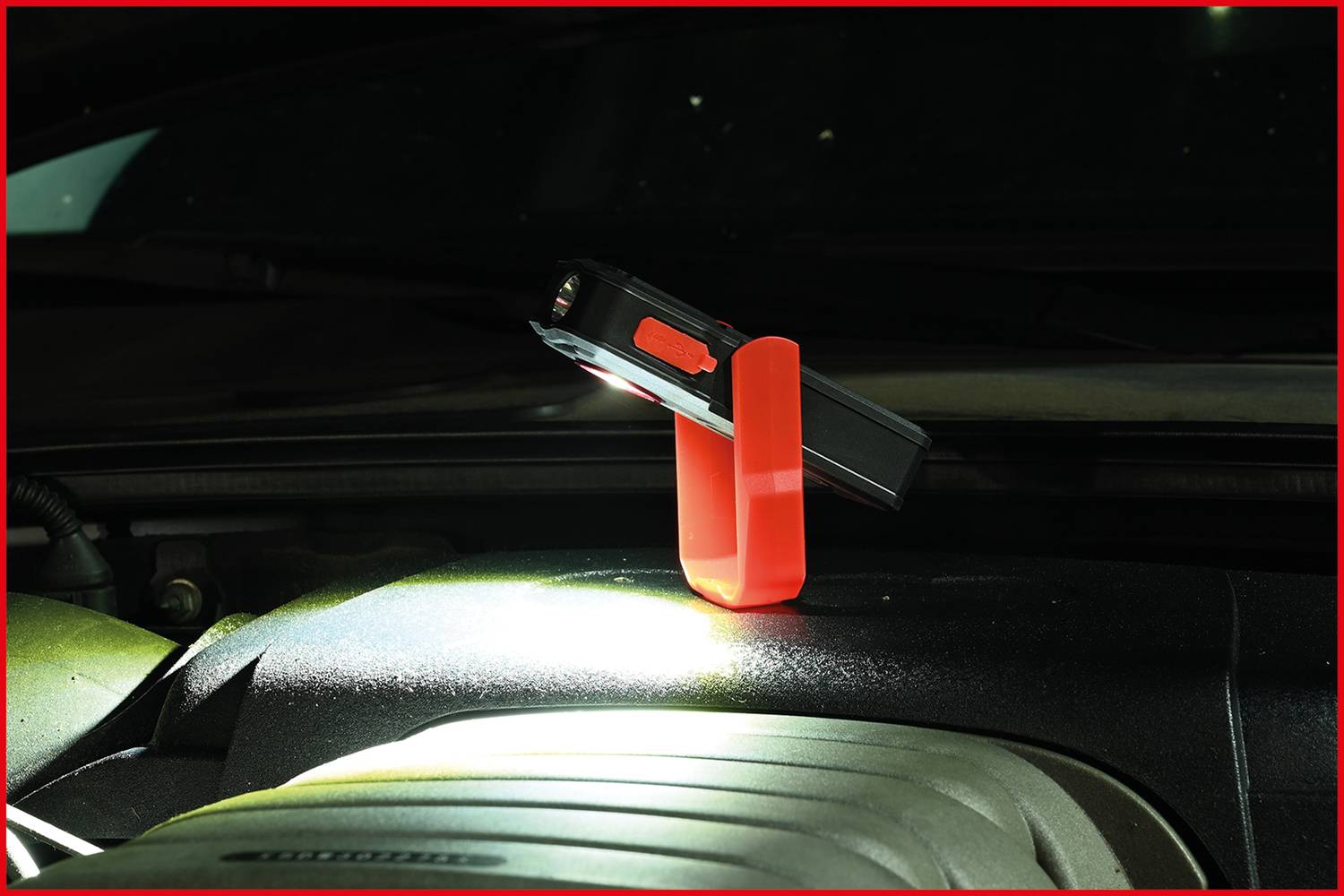 Kapesní svítilna stojí šikmo na červeném držáku a svítí na motor automobilové součástky.