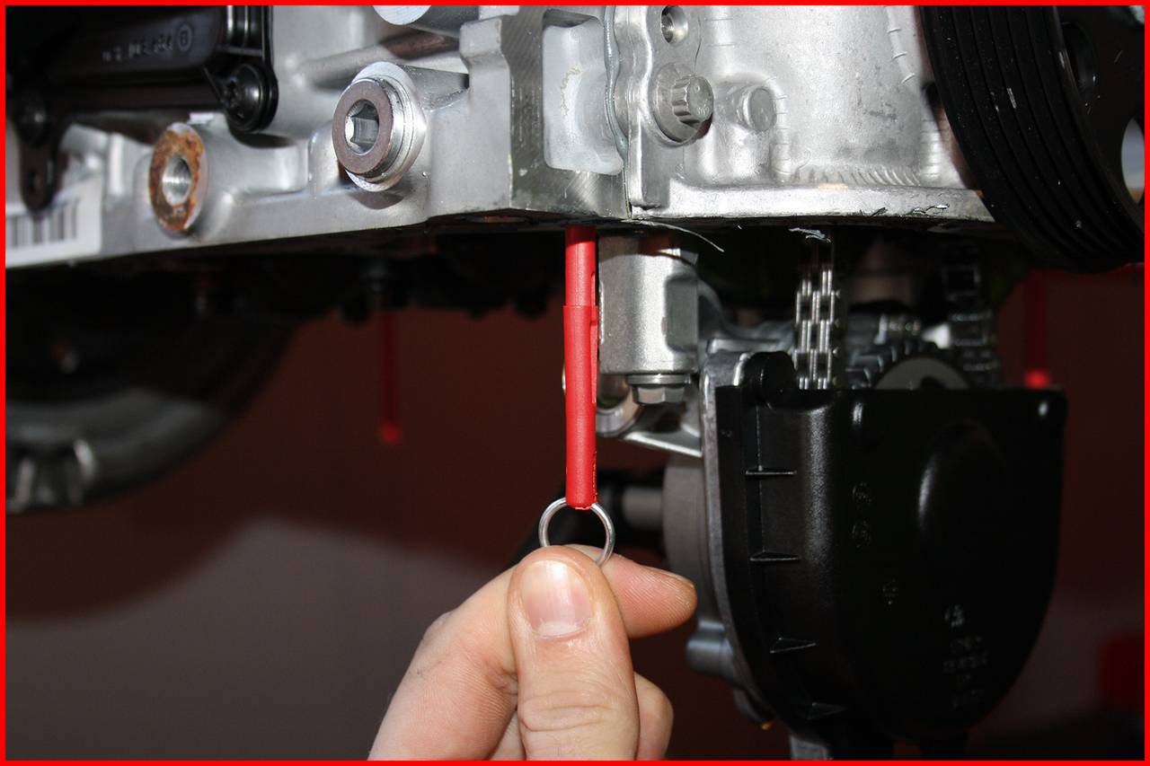 Ruka vytahuje červenou měrku oleje, detailní záběr motoru s rukou kontrolující měrku. Důležité pro údržbu.