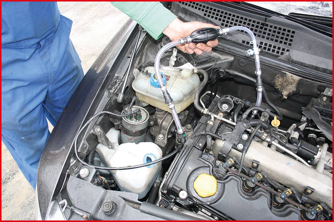 Mechanik kontroluje motor automobilu. Je vidět ruka, která používá hadice ke kontrole brzdové kapaliny.