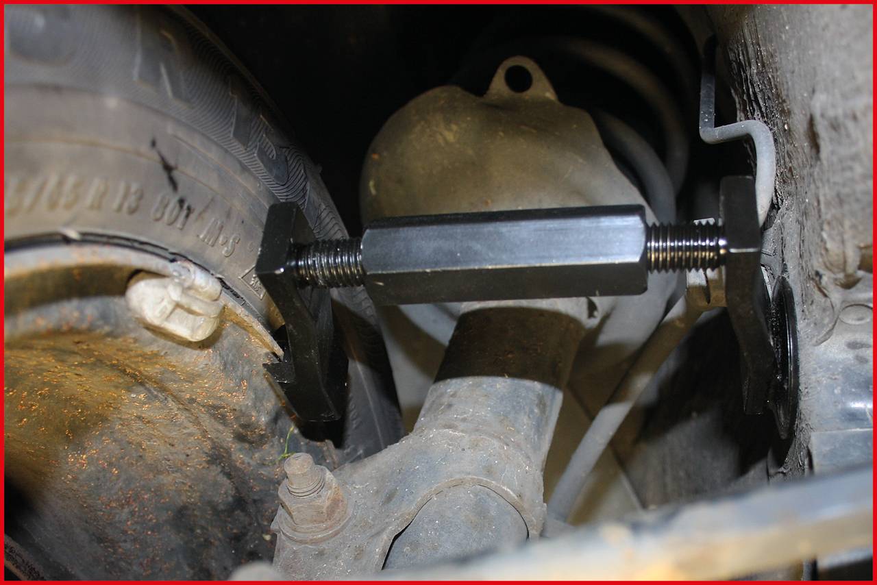 Pneumatika automobilu poblíž tlumiče, upevněná svěrkou. Okolí zobrazuje mechanické díly vozidla.