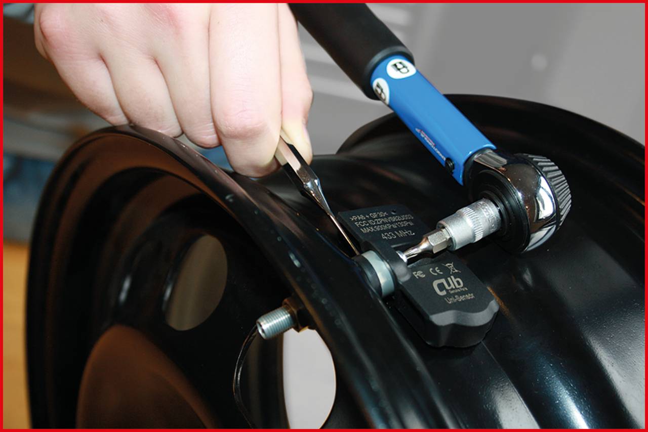'Ruční montáž TPMS senzoru na ráfek pomocí nástroje; detailní záběr instalace.'