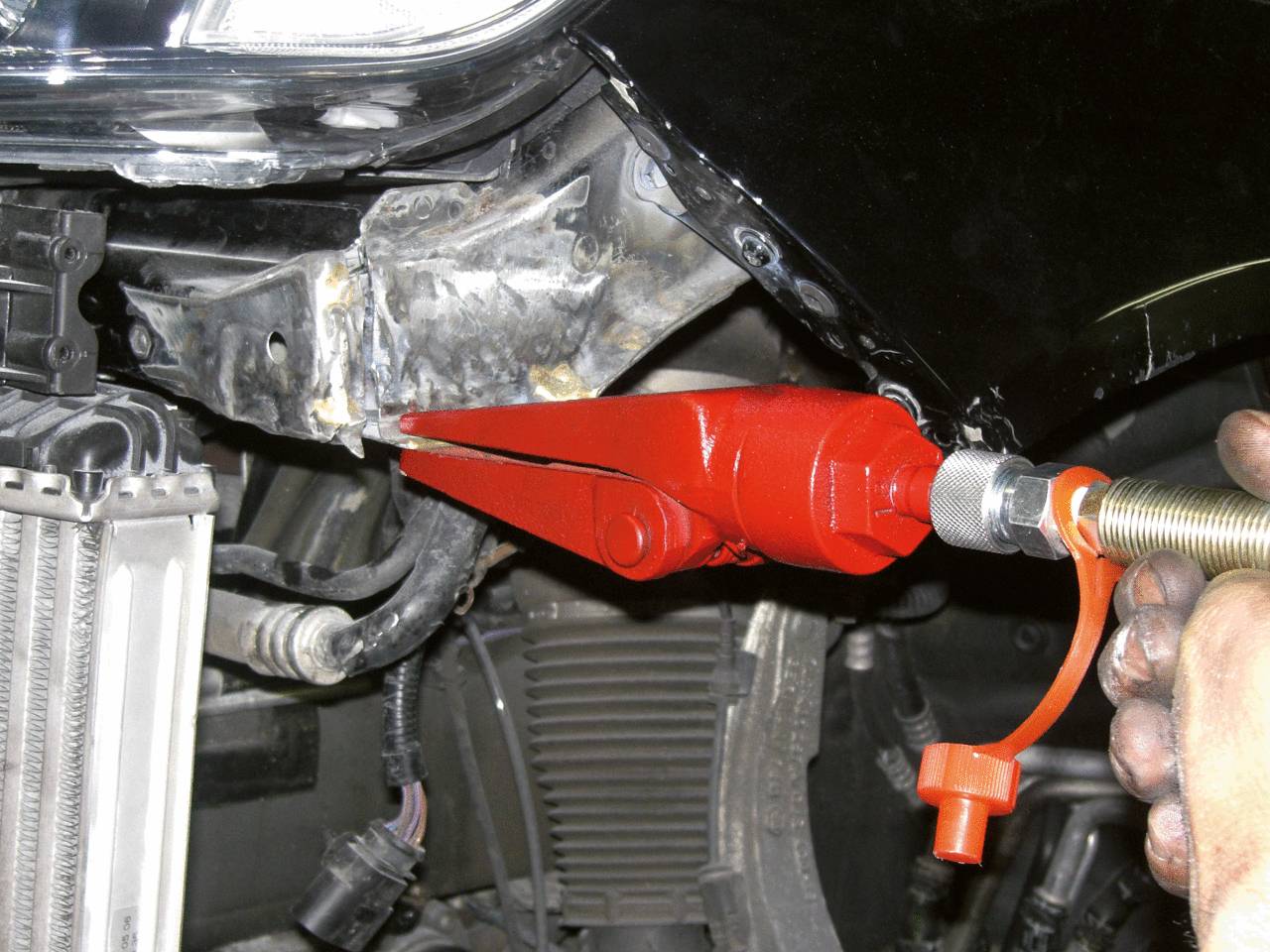 Červený přípravek se používá k opravě části karoserie automobilu. Jedna ruka drží nástroj, aby vyvinula tlak.