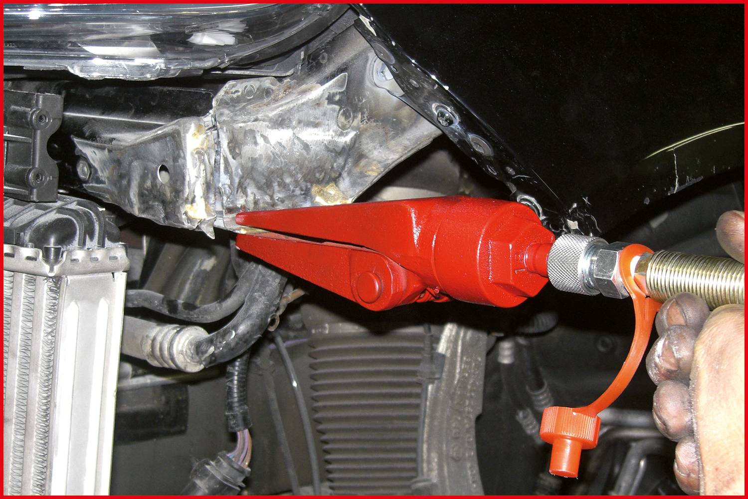 Červená upínací svorka je připevněna k dílu automobilu. Mechanik pevně drží rukojeť nástroje.
