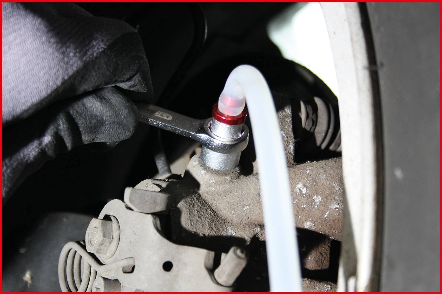 Mechanik utahuje šroub pomocí klíče na vozidle. Průhledná hadice je připojena k šroubu.