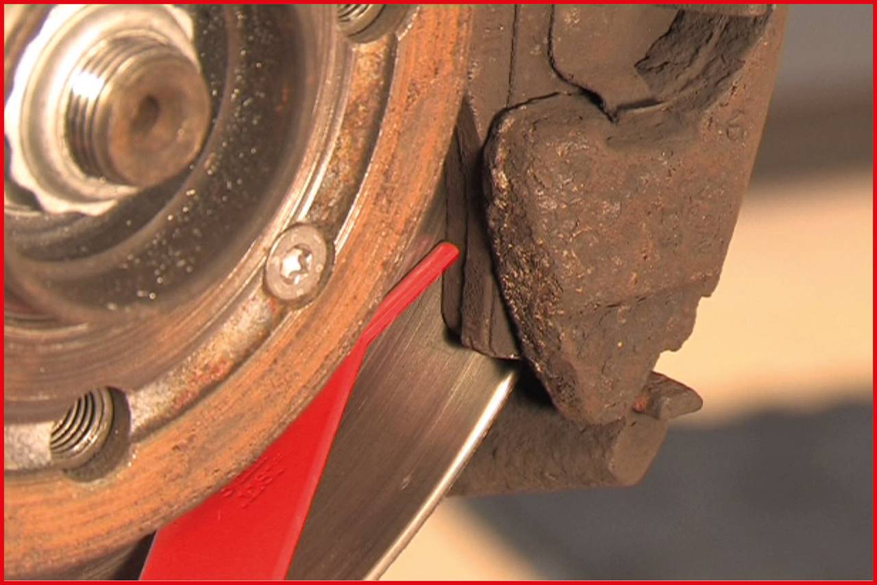 Detailní záběr brzdového kotouče a scéna výměny brzdových destiček. Obrázek jasně zobrazuje brzdovou destičku v průběhu výměny.