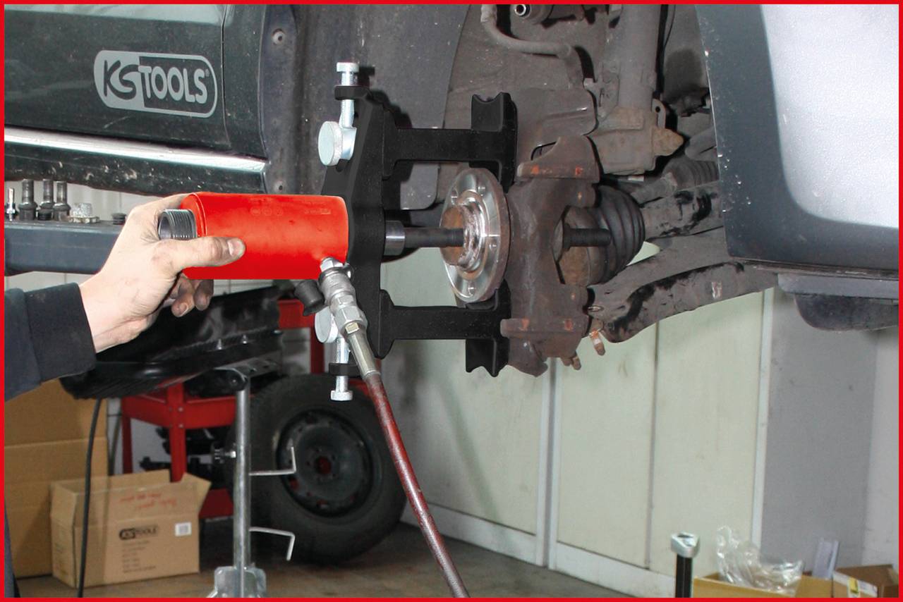 Osoba používá hydraulický nástroj k demontáži brzdového kotouče na automobilu. Pozornost je soustředěna na mechanický postup.