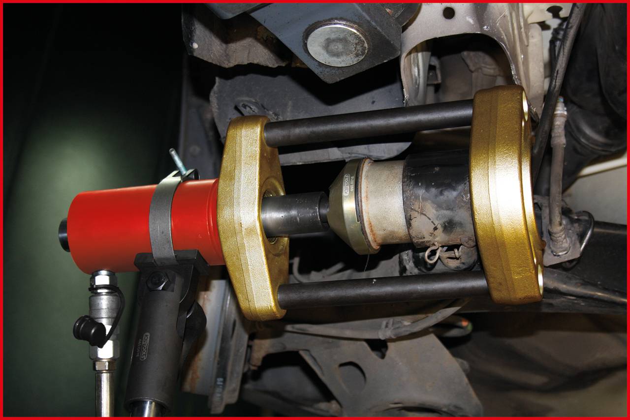 Hydraulický nástroj odstraňuje pouzdro z části zavěšení vozidla. Používá se červený hydraulický válec.