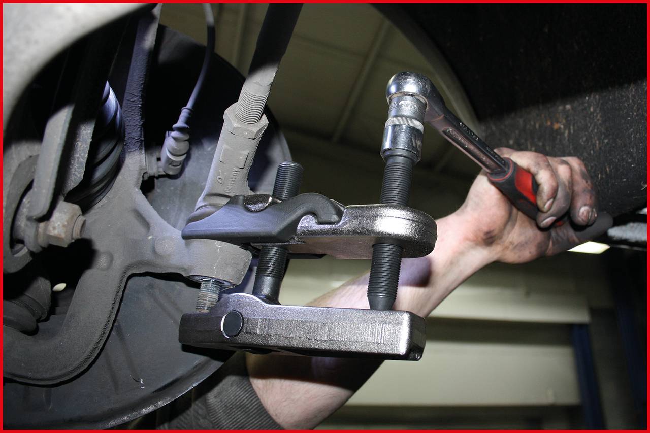 Osoba opravuje brzdy automobilu, používá klíč a C-svorku v autoservisu. Důraz je kladen na použití nářadí.