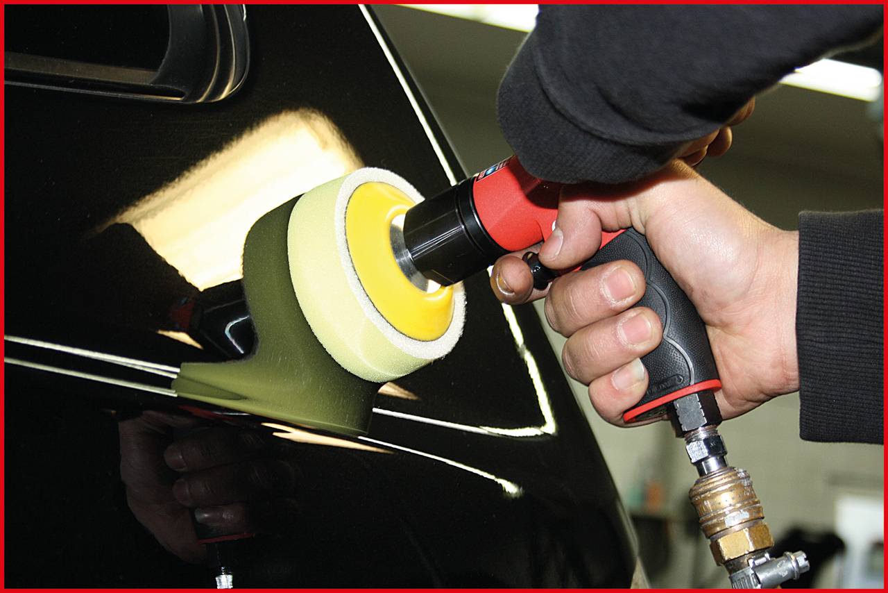 Člověk leští lesklý černý lak automobilu pomocí leštičky v autoservisu.