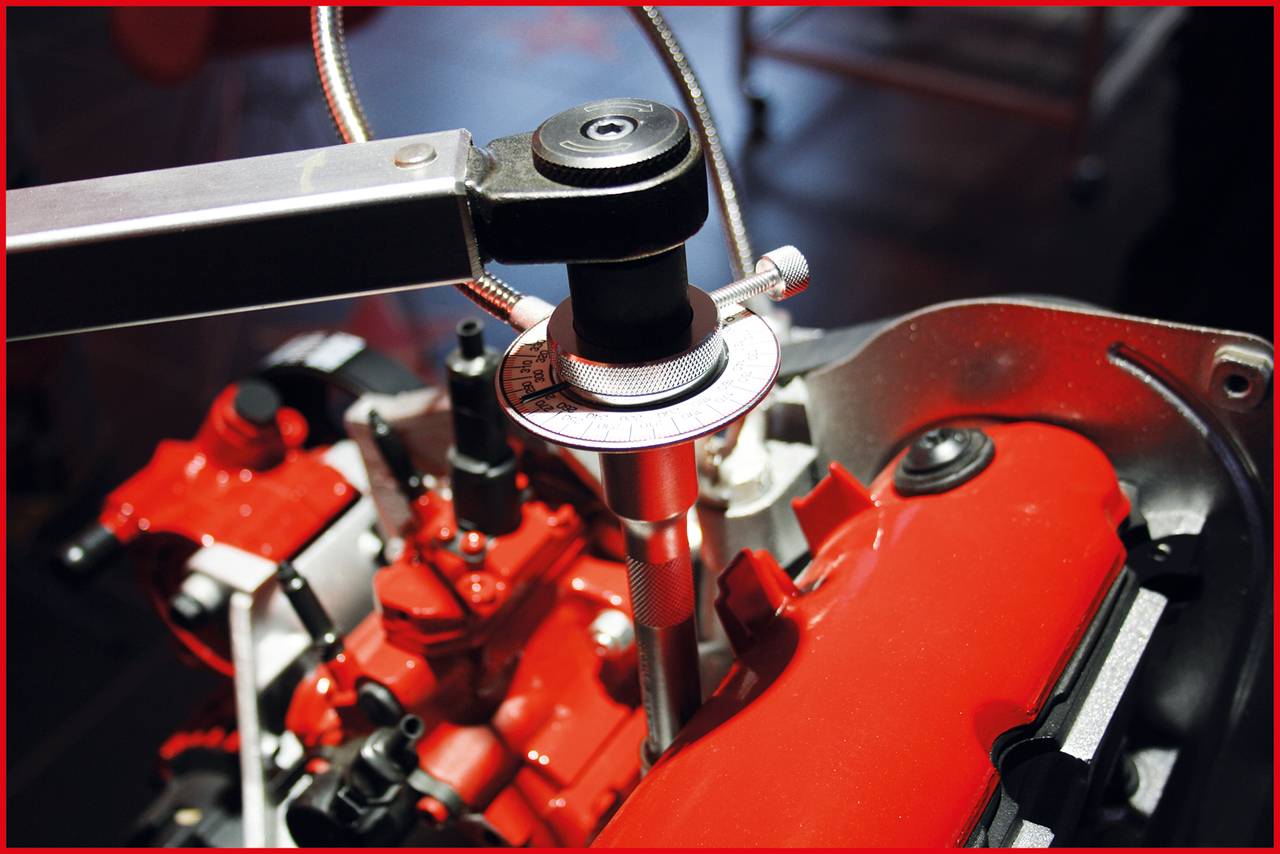 Červený motor je seřizován pomocí nástroje. Měřicí přístroj ukazuje přesná nastavení. Mechanické detaily jsou viditelné.