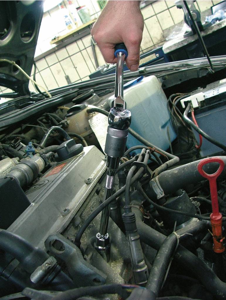 Osoba utahuje šrouby momentovým klíčem v motorovém prostoru automobilu.