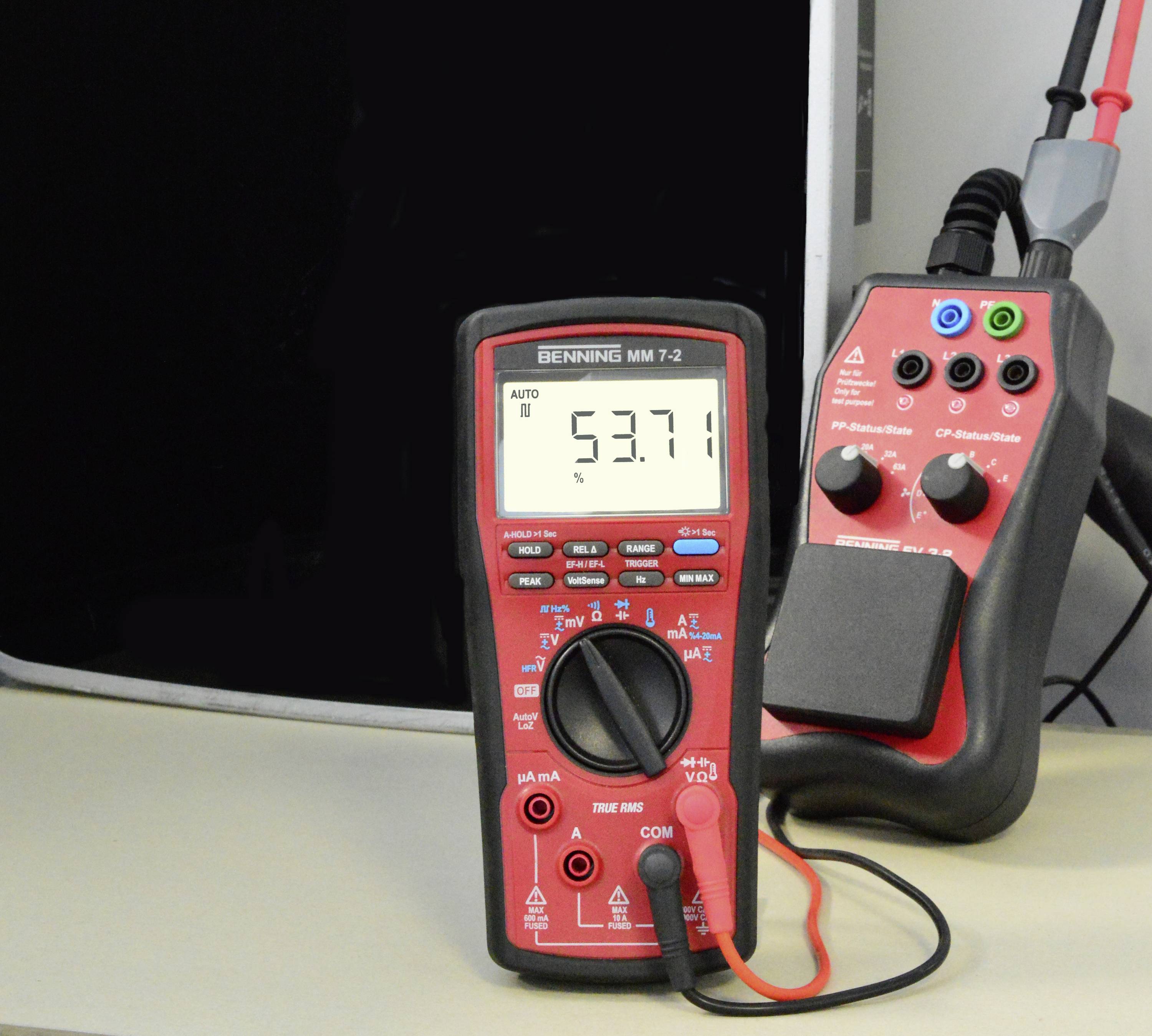 Multimetr měří napětí 5,371 V. Stojí na stole vedle dalšího elektrického přístroje s kabely.
