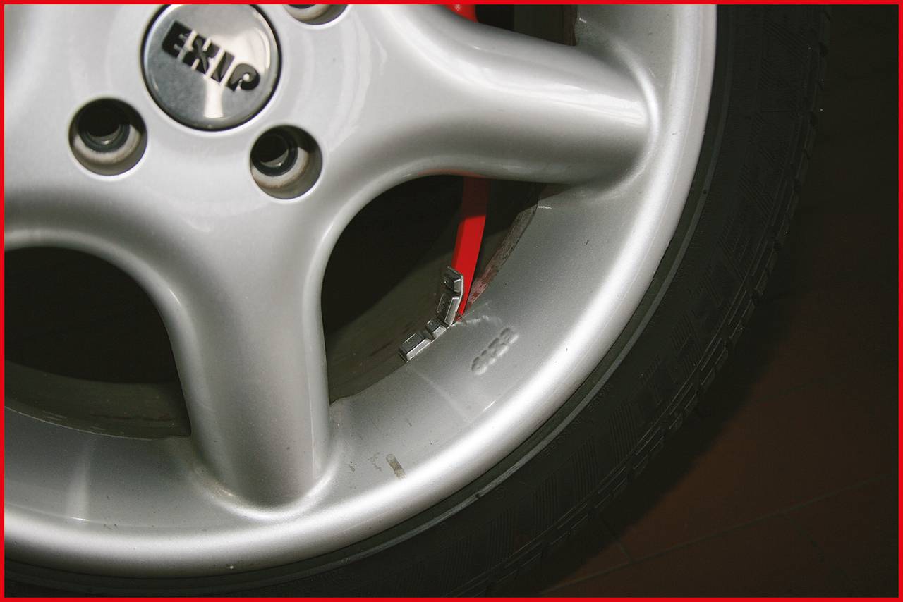 Detailní záběr automobilového pneumatiky se stříbrným hliníkovým diskem a viditelným vyvažovacím závažím na okraji. Na ráfku je viditelný text 'EHKP'.