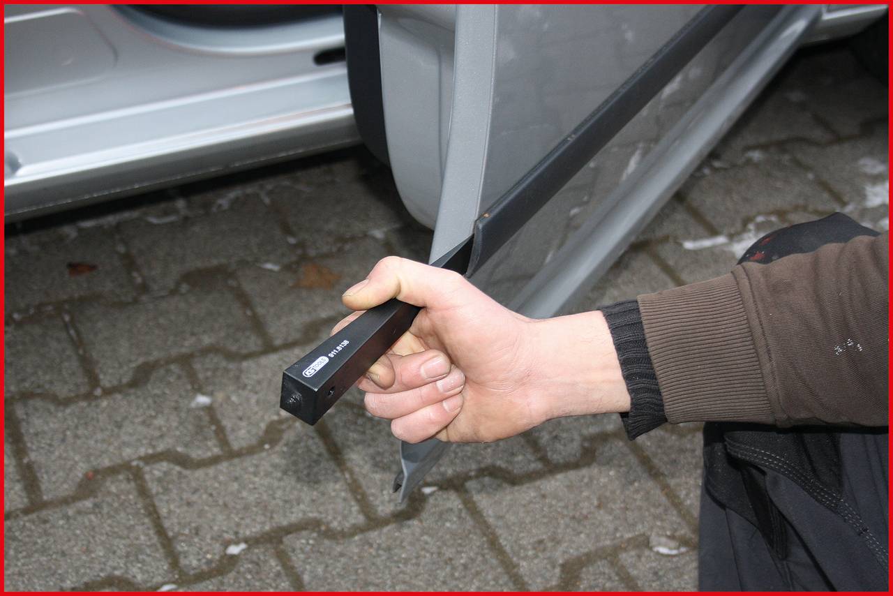 Osoba drží zařízení, které je připevněno k otevřenému zámku automobilu. Zařízení vypadá, že je určeno k odemykání zámků.