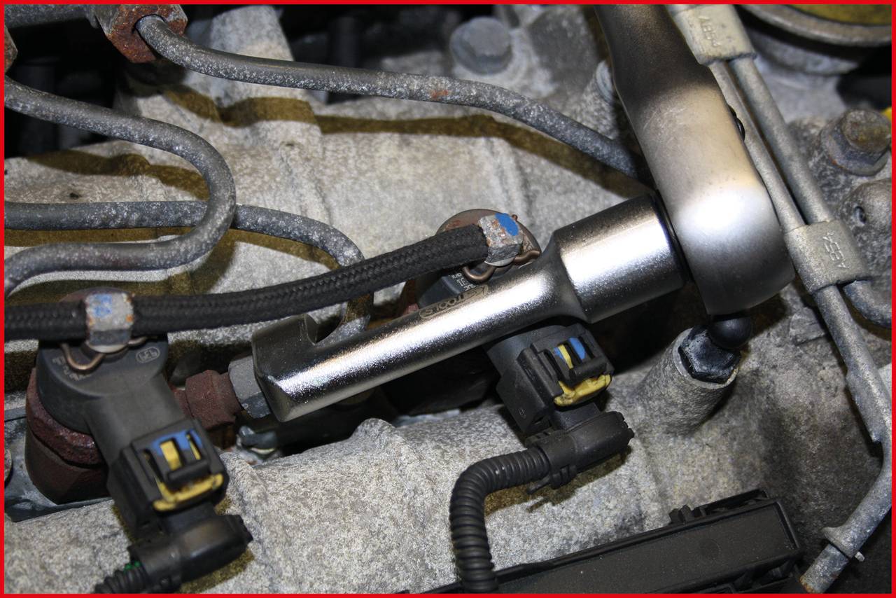 Detailní záběr části automobilu s několika kovovými trubkami a elektrickými konektory v motorovém prostoru. Kabely jsou připojeny.