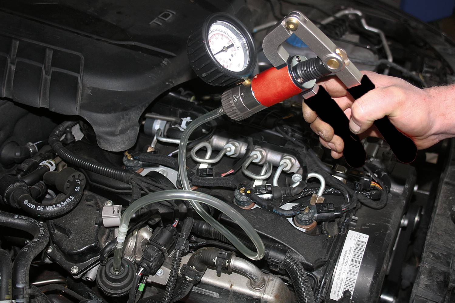 Ruka používá ruční pumpu s manometrem k testování tlaku v palivovém systému otevřeného automobilového motoru.