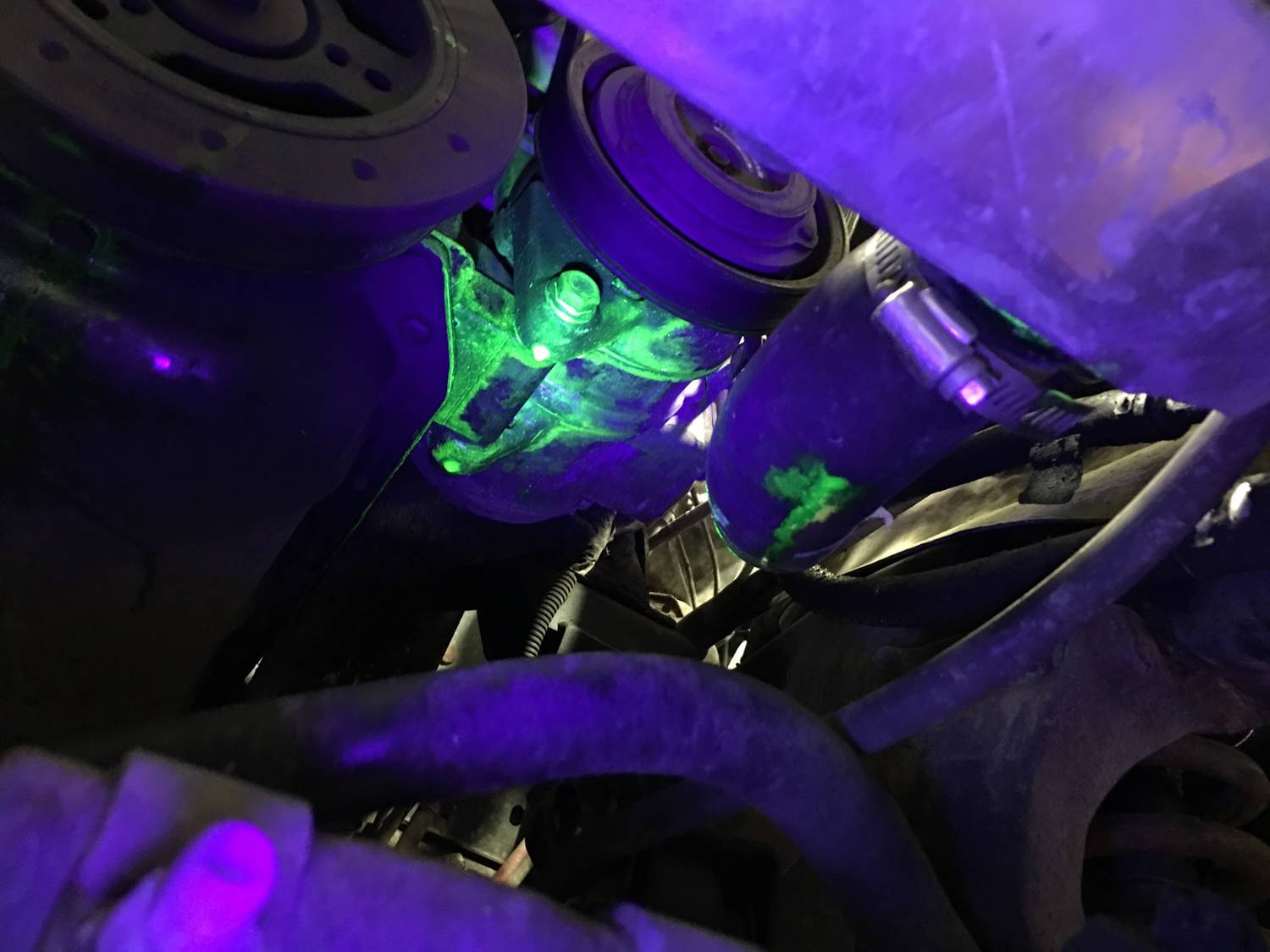 Hledání netěsnosti v motorovém prostoru pomocí UV světla: Fluoreskující zelené skvrny označují místo úniku na jedné součástce.