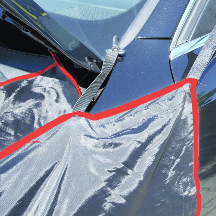 Auto s plachtou upevněnou na čelním skle. Plachta má červené okraje a chrání před povětrnostními vlivy.