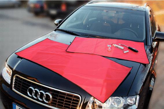 Černé auto s červenými hadry na kapotě; vedle leží nářadí.