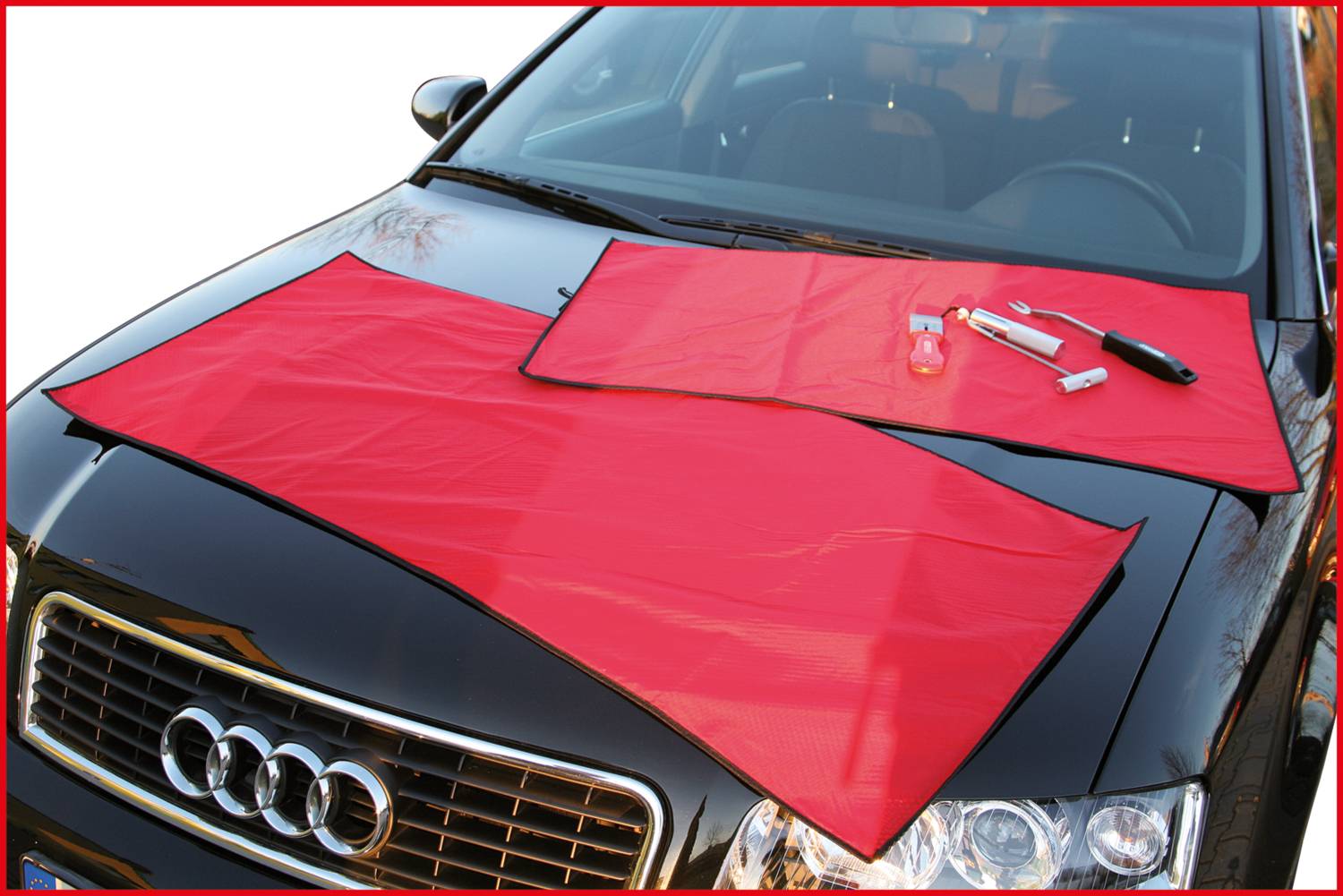 Červený ochranný potah na černé karoserii automobilu, s několika nástroji umístěnými na něm.
