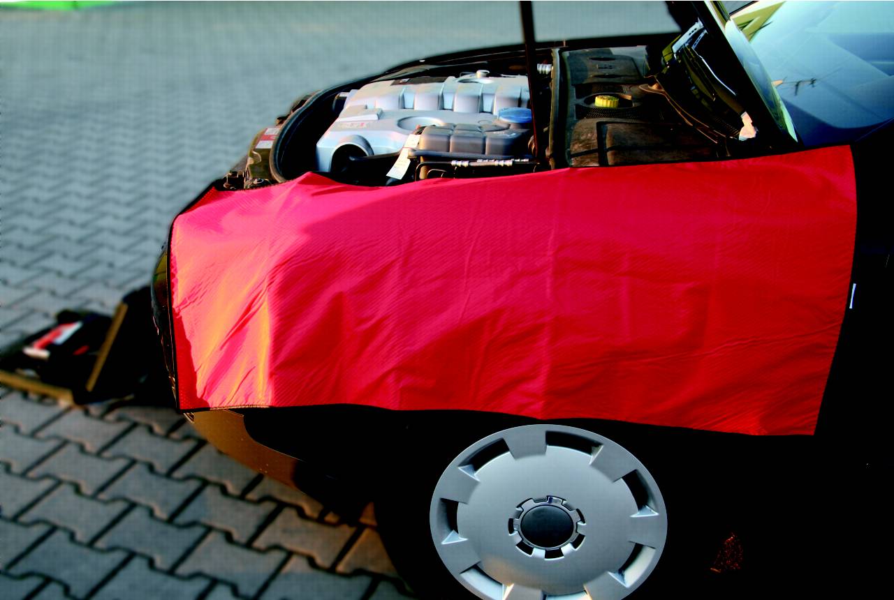 Auto s otevřenou kapotou, červená ochranná plachta zakrývá přední blatník, zaparkované na dlážděné ploše.