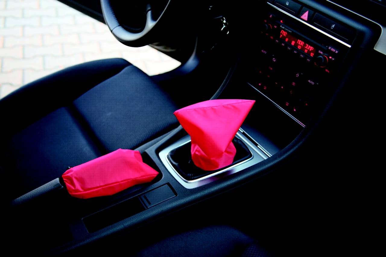 Interiér automobilu s černými sedadly; řadicí páka a ruční brzda jsou kryty zářivě růžovými obaly.