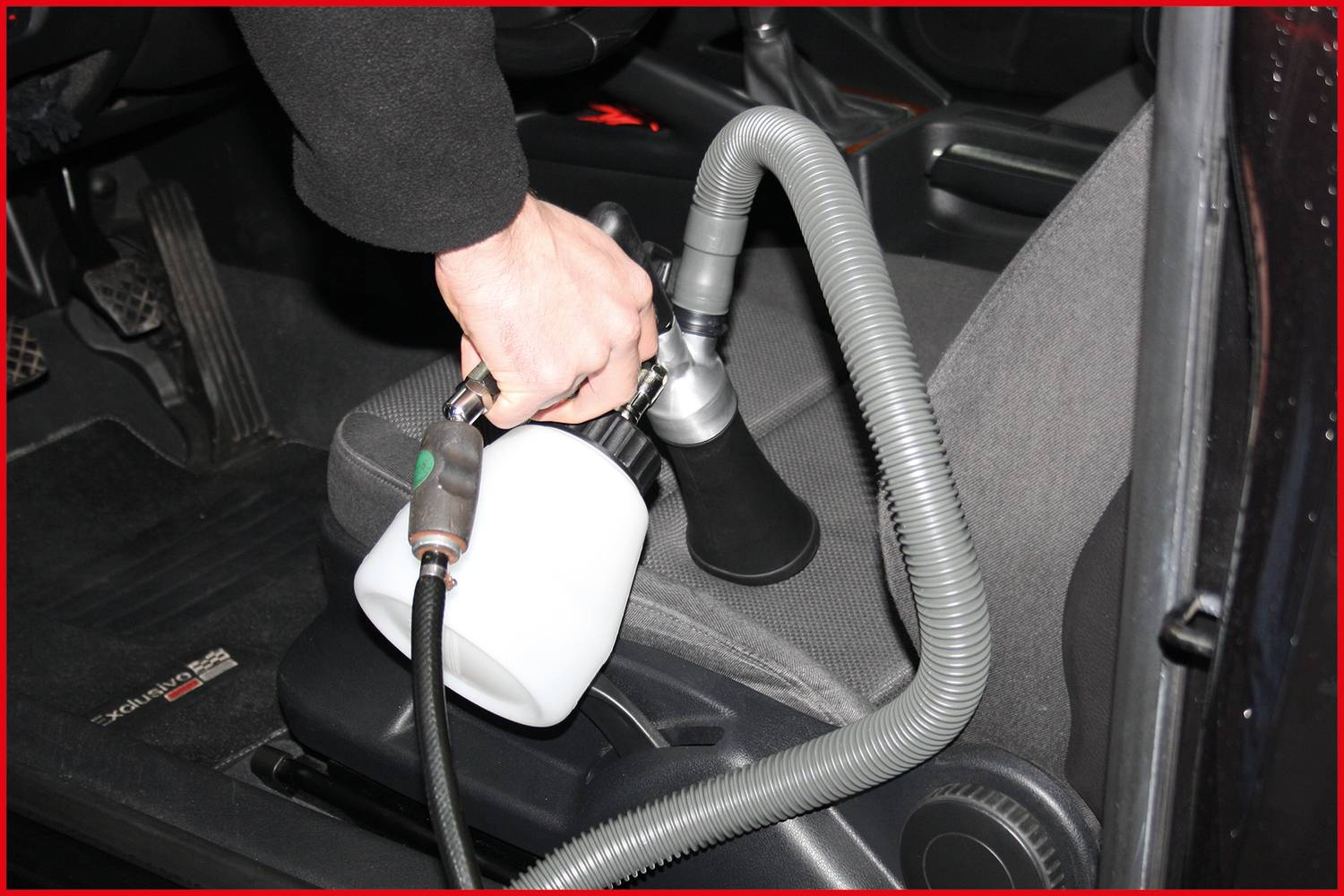 Osoba čistí autosedačku sprejem a hadicí, aby odstranila nečistoty.