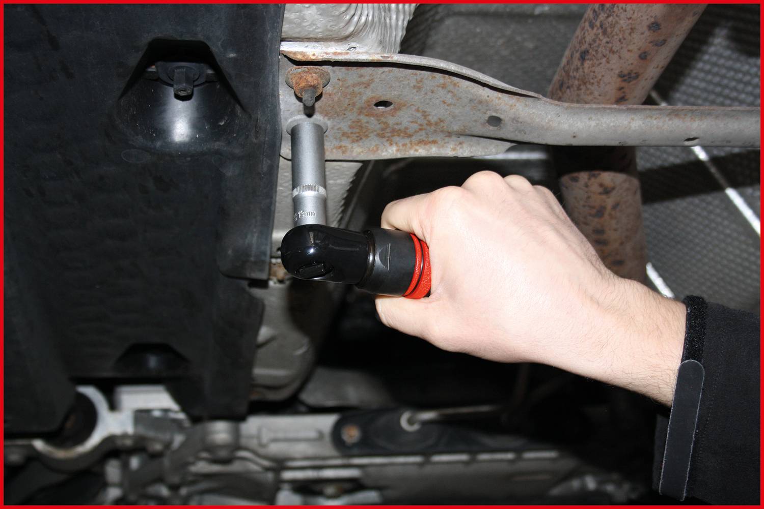 Jedna ruka drží nástroj, který pracuje na spodní straně automobilu. Klíč se používá k povolení šroubu.