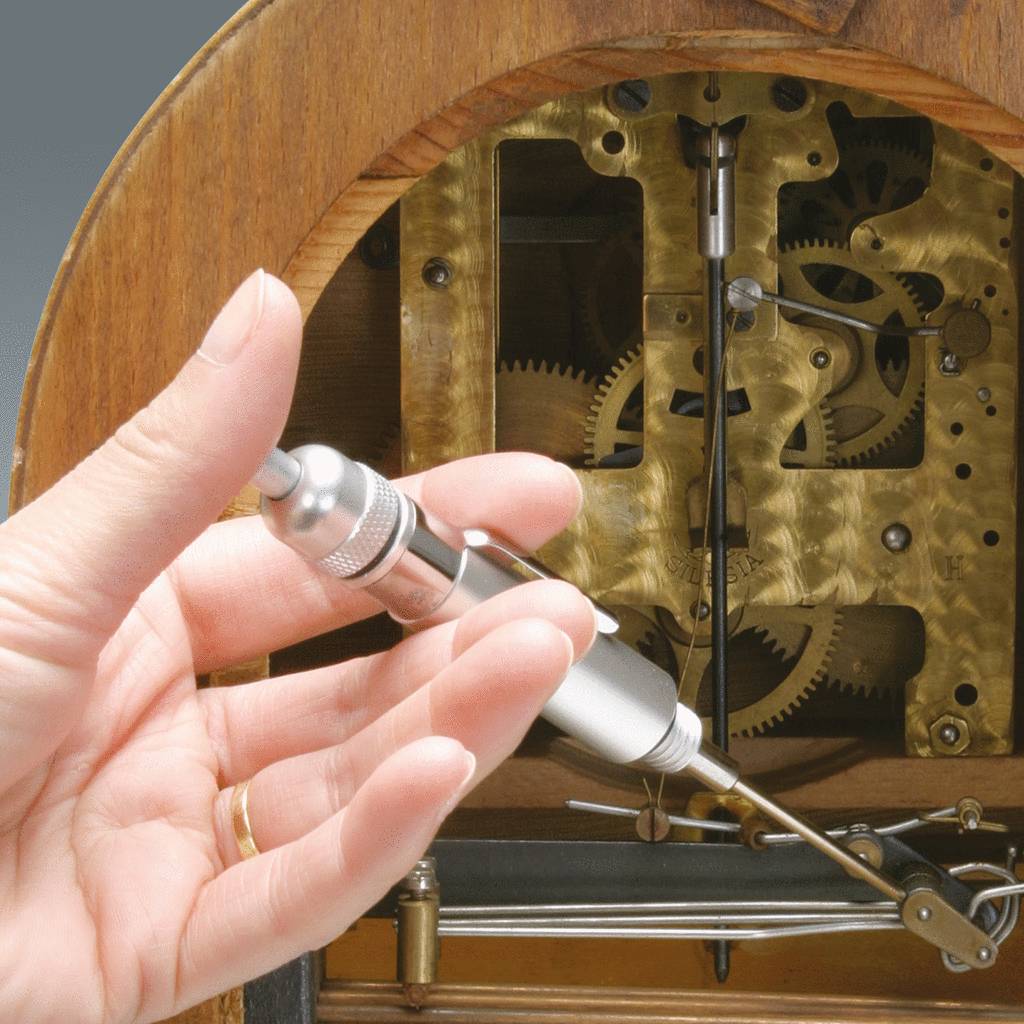 Ruka obsluhuje přesný měřicí přístroj před složitým hodinovým strojkem, který odhaluje ozubená kola a mechanismy.