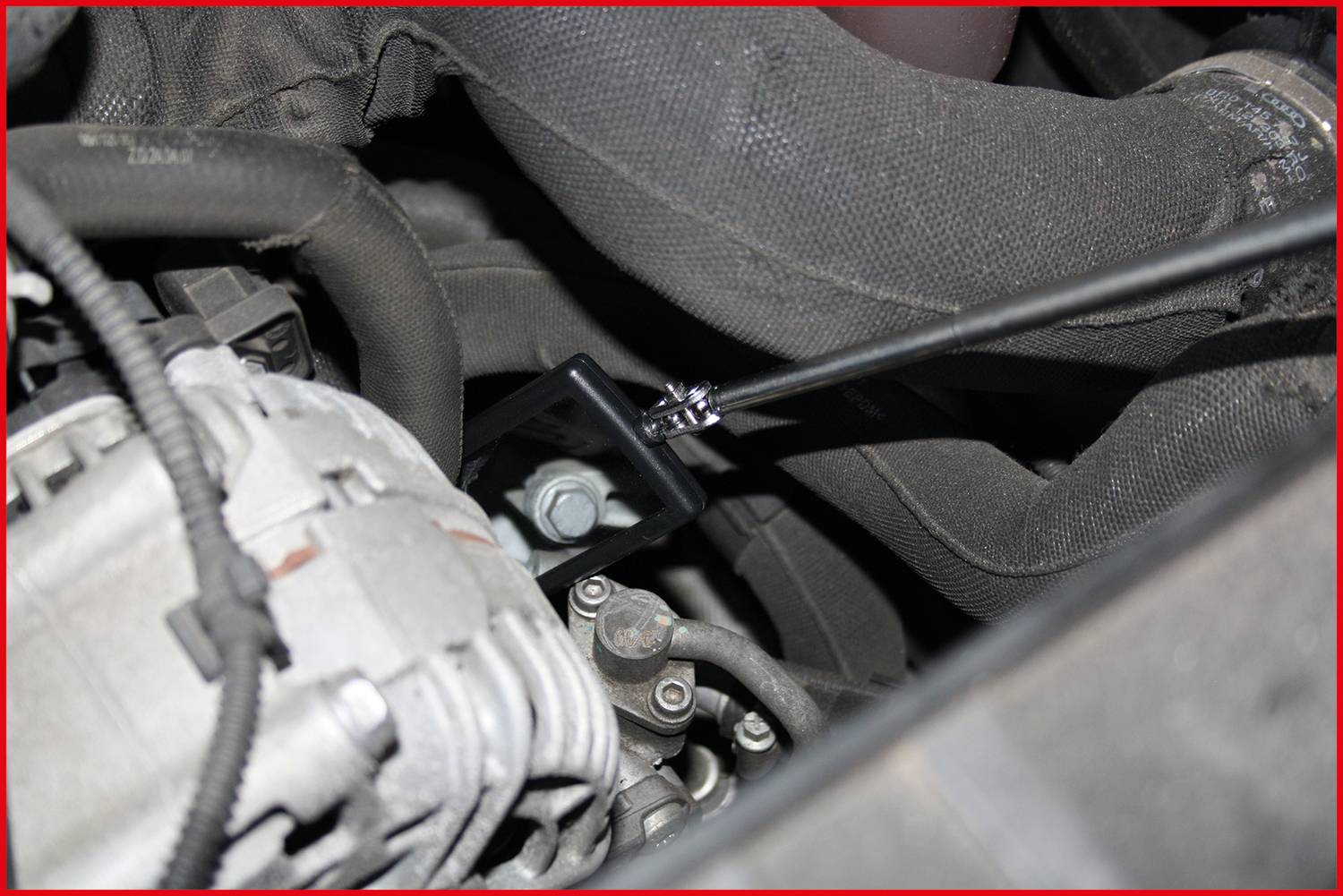 Detailní záběr motorového prostoru s kovovým čepem obklopeným černým kabelem. Část motoru je viditelná v pozadí.