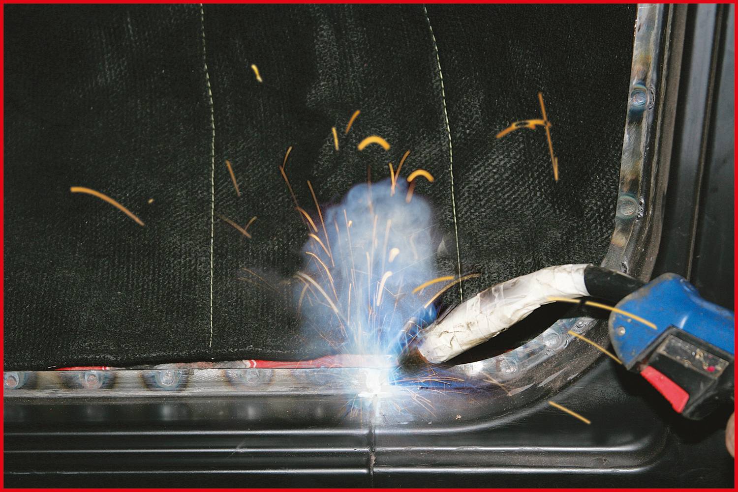Svařovací přístroj vytváří jiskry a kouř, když pracuje na kovovém dílu. Pozadí je rozmazané.
