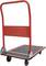 Červený plošinový vozík s černou protiskluzovou plochou a čtyřmi kolečky, vhodný pro přepravu těžkých předmětů v skladových prostorech.
