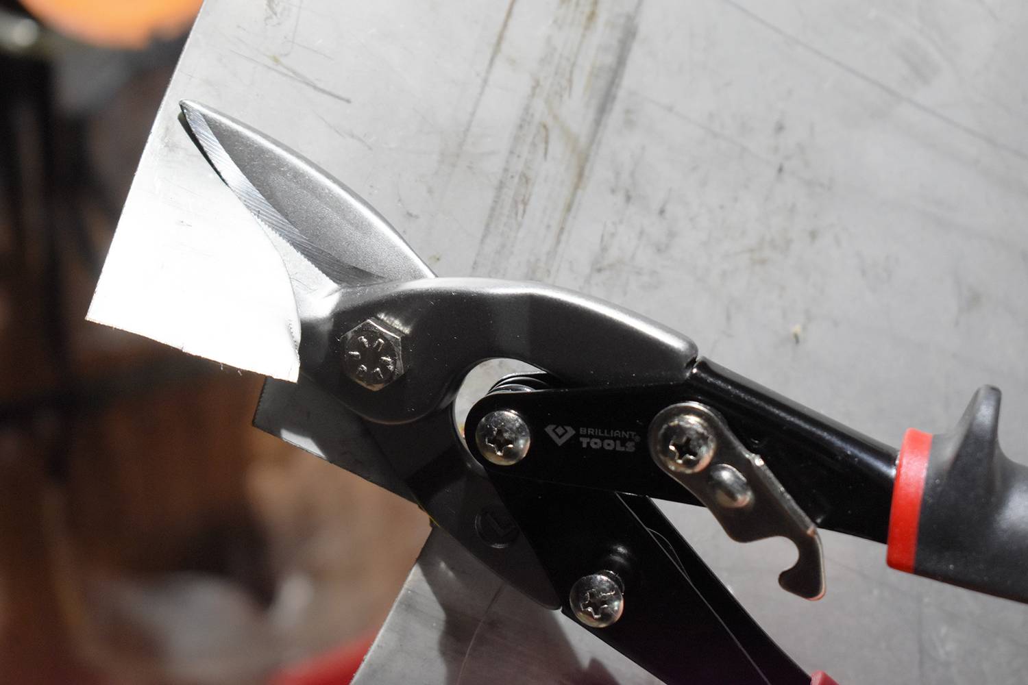 Nůžky na plech stříhají kovový kus, detail zblízka. Nůžky mají černé rukojeti a přesně prostřihávají materiál.