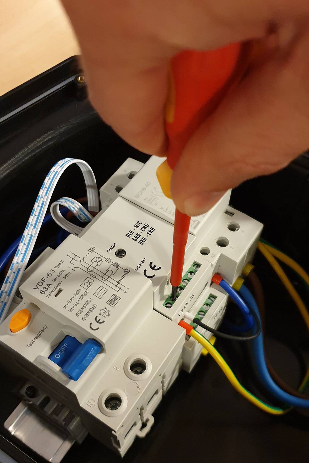 Ruka používá šroubovák k upevnění elektrických připojení v rozvaděči. Barvy vodičů: modrá, zelená, žlutá.