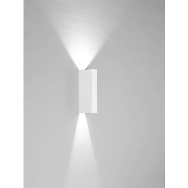 Nástěnná lampa s moderním designem vyzařuje světlo nahoru a dolů a vytváří jemné světelné kužely na šedé stěně.