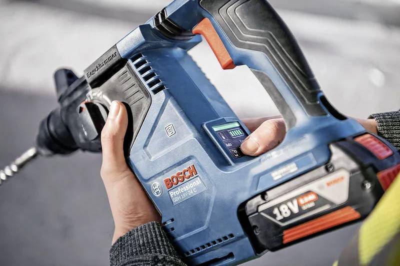 Osoba drží modrou 18V aku vrtačku Bosch Professional, zaměřuje se na úchop a vrtací bit, což naznačuje použití ve stavebnictví nebo při domácích kutilských pracích.