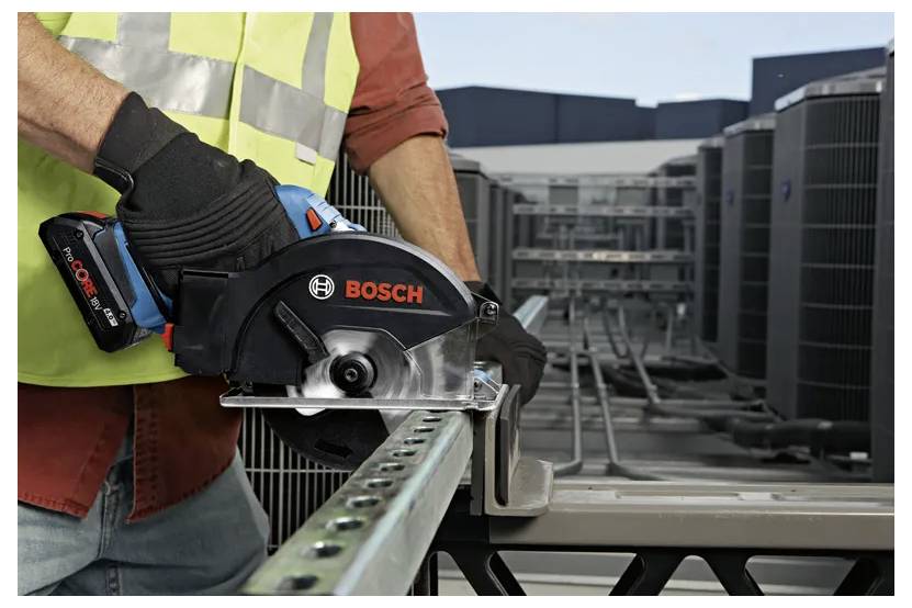Osoba v bezpečnostní vestě a rukavicích používá přenosnou elektrickou pilu Bosch k řezání kovového zábradlí na střeše poblíž jednotek HVAC.