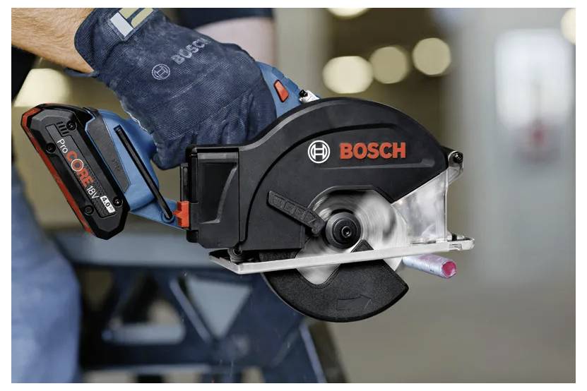 Osoba držící elektrickou pilku od společnosti Bosch, která řeže kovovou tyč. Pilka je vybavena baterií CORE18V a je používána v průmyslovém prostředí.