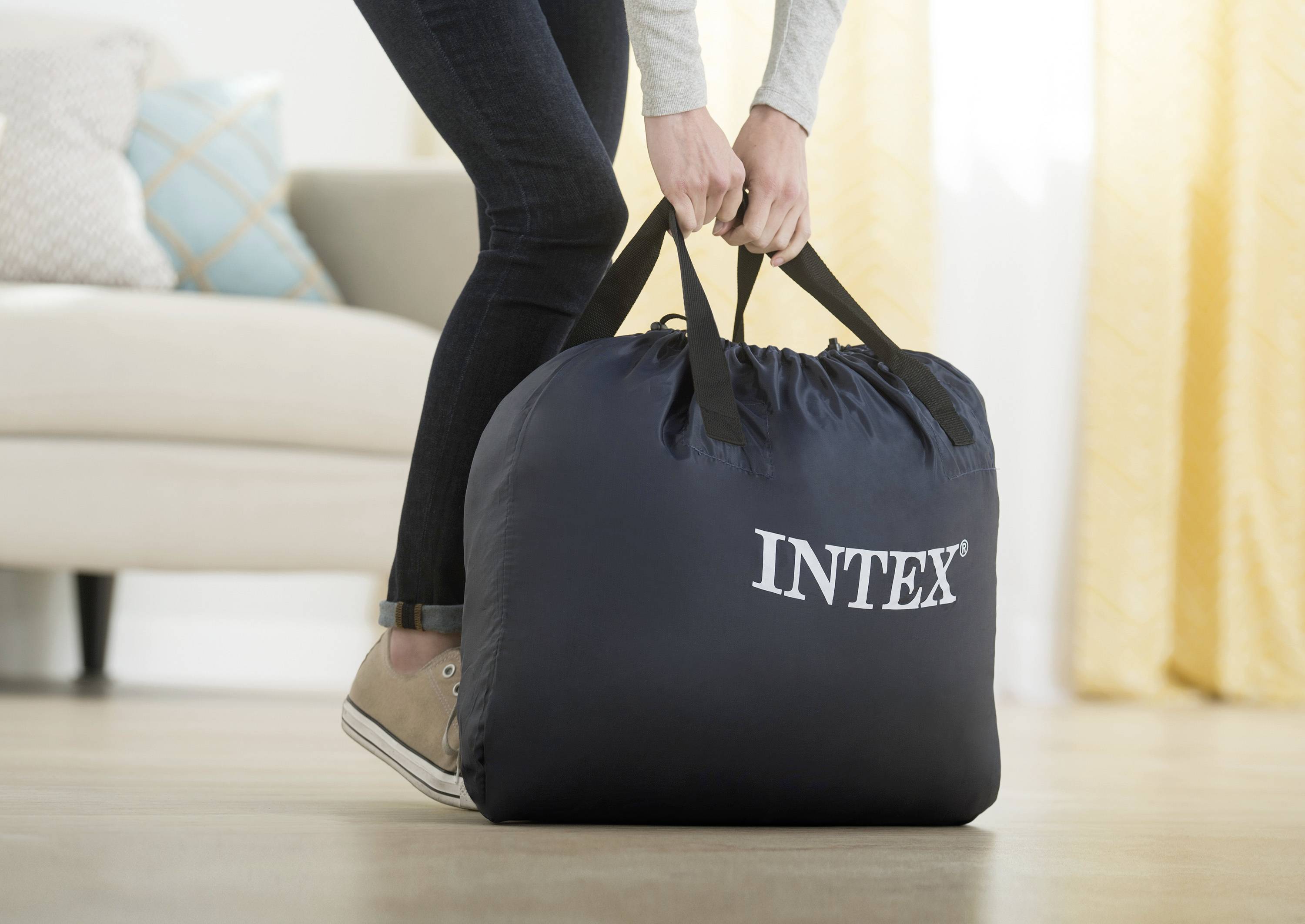 Jedna osoba zvedá velkou černou tašku s nápisem 'INTEX' ze země. Taška vypadá, že je těžká.